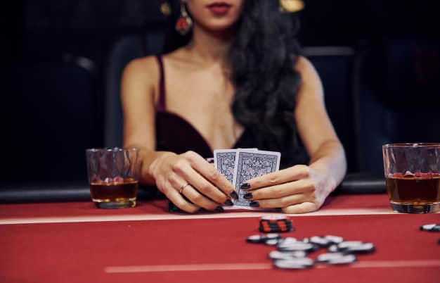 une femme avec un long ahir noir tenant des cartes de casino dans ses mains avec des jetons de poker à côté d'elle